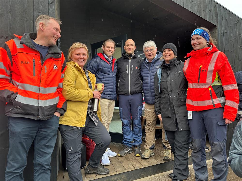 En blid gjeng står oppstilt på trappa til dagsturhytta og smiler til hverandre og til kamera. F.v. Rolf Inge Pettersen (Grimstad kommune), Karin Glomsaker (Grimstad kommune), Jan Gordon Tobiassen (SpareBank 1 SR-Bank), Bård Andreas Lassen (prosjektleder i Agder fylkeskommune) Arne Thomassen (fylkesordfører), Janne Leithe (Grimstad kommune) og Pernille Sandemose (Grimstad kommune).  - Klikk for stort bilde